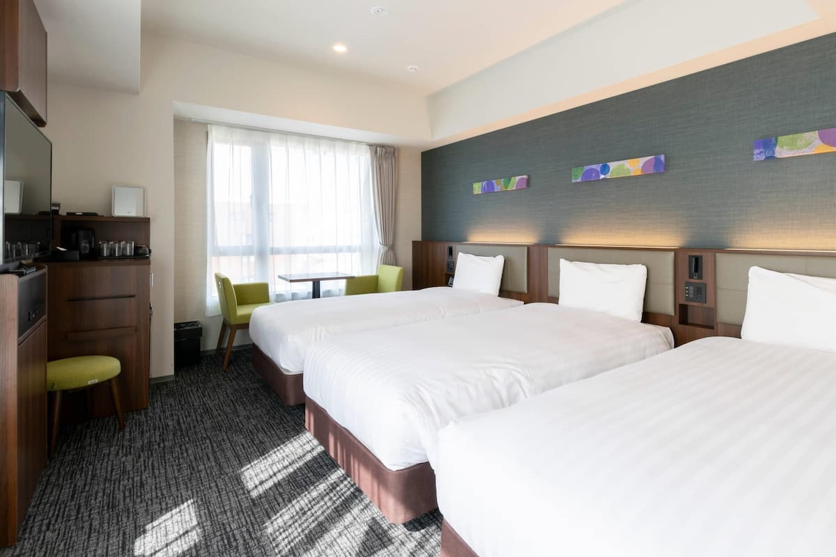 Habitación de hotel con dos camas, un escritorio, una silla y una ventana con cortinas.