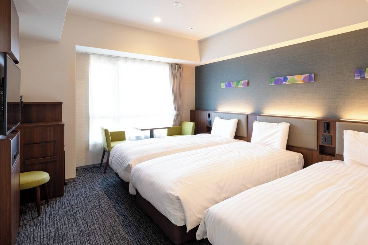 Une chambre d’hôtel avec deux lits, un bureau, une chaise et un téléviseur.