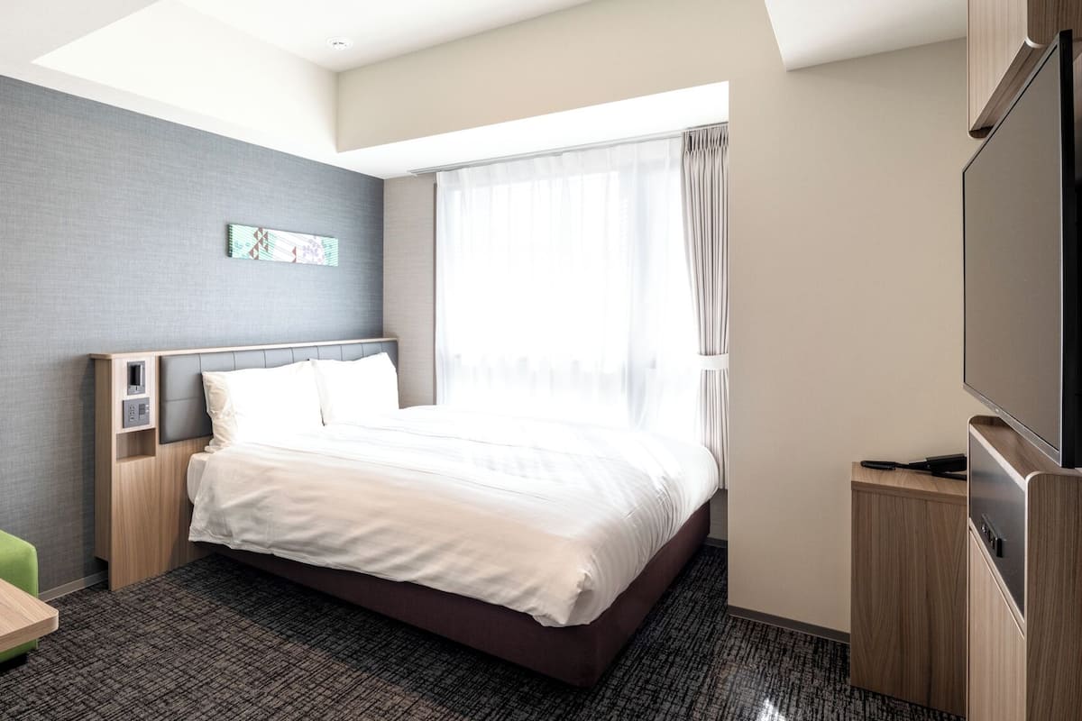 Une chambre d’hôtel avec un lit, un bureau, une télévision et une fenêtre avec des rideaux.
