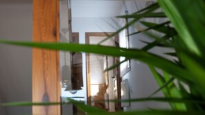Uma escadaria de madeira com piso ladrilhado leva a um quarto com parede branca e luminária pendente.