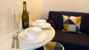 Un pequeño comedor con una mesa preparada para dos personas, incluyendo copas de vino, una botella de Prosecco y cuencos.