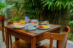 Una mesa de comedor con alimentos para el desayuno, un vaso de jugo de naranja y una botella de agua.