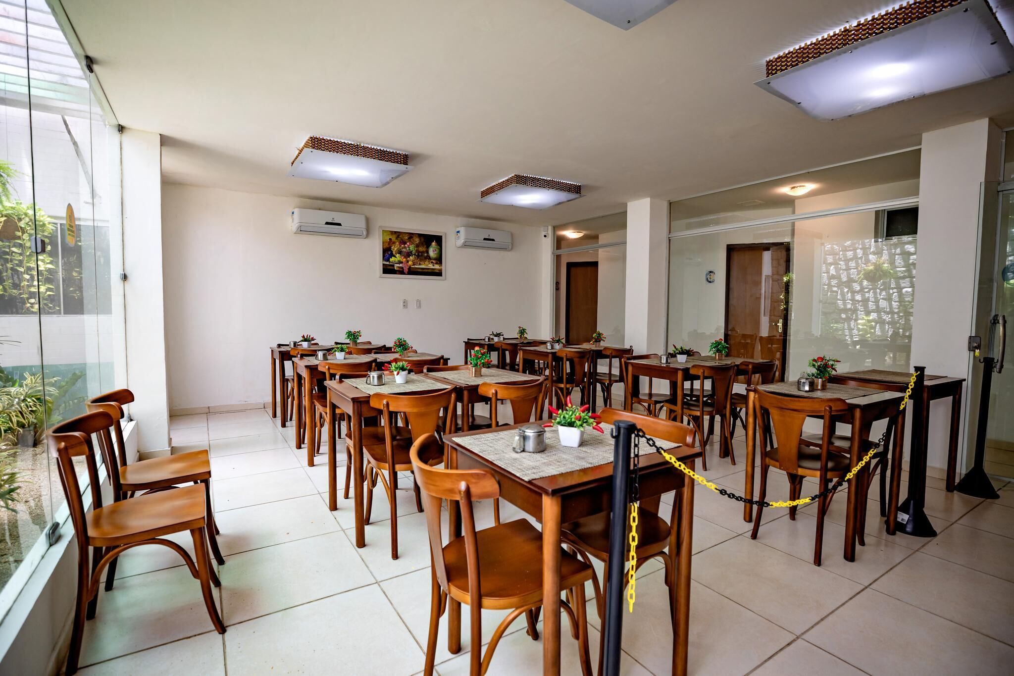 A dining area with multiple tables and chairs, air conditioning units on the ceiling, and a view through a glass door.