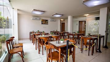 Un comedor con varias mesas y sillas, unidades de aire acondicionado en el techo y vistas a través de un ventanal.