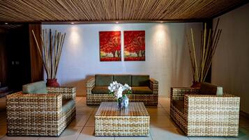A room with wicker furniture, a central coffee table, and two paintings on the wall.