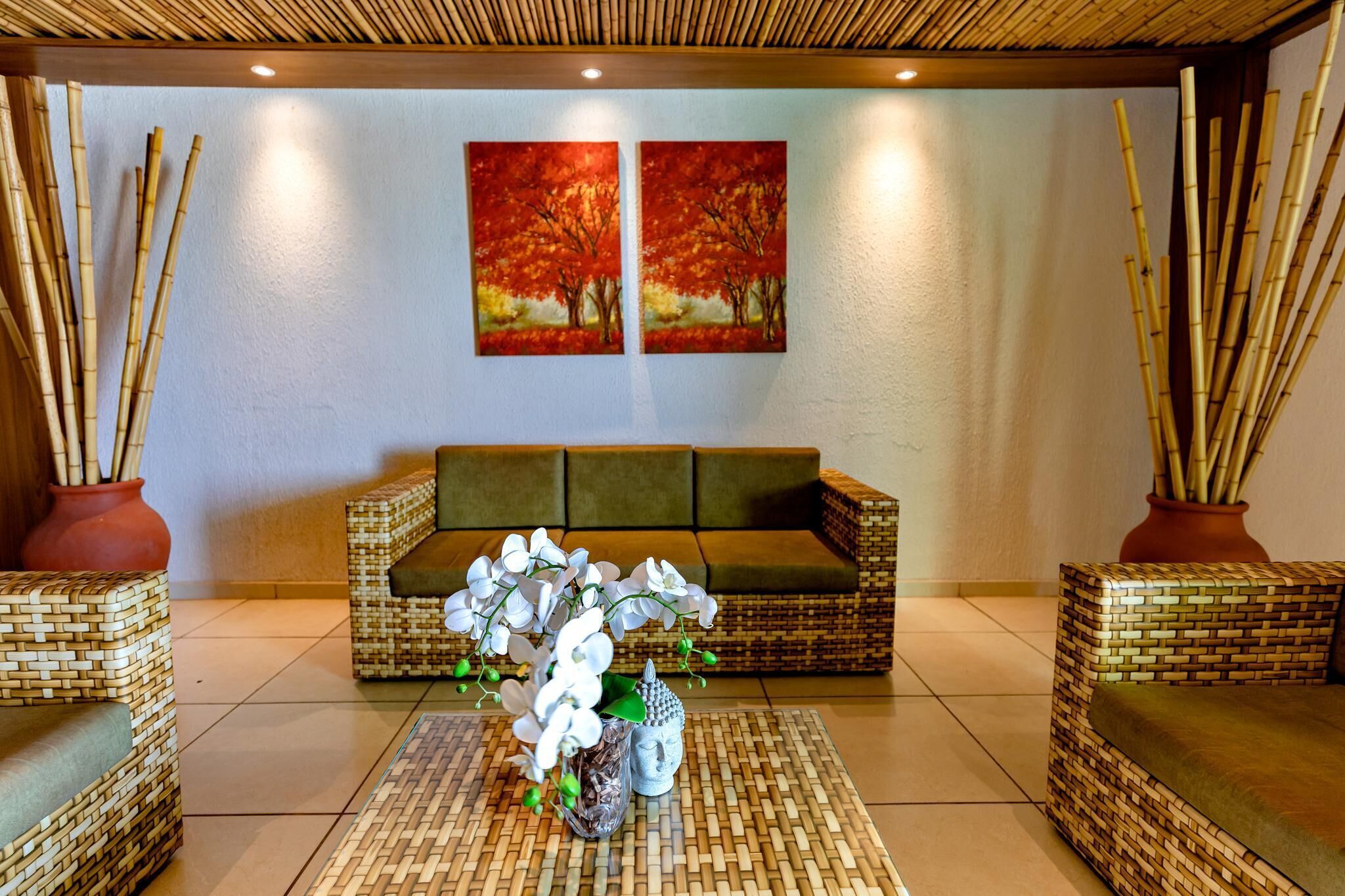 Um hall com um sofá de palha, dois vasos com galhos de bambu e uma mesa com flores brancas.