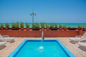 Una piscina con vista al mar, rodeada de plantas en macetas y sillas de descanso.