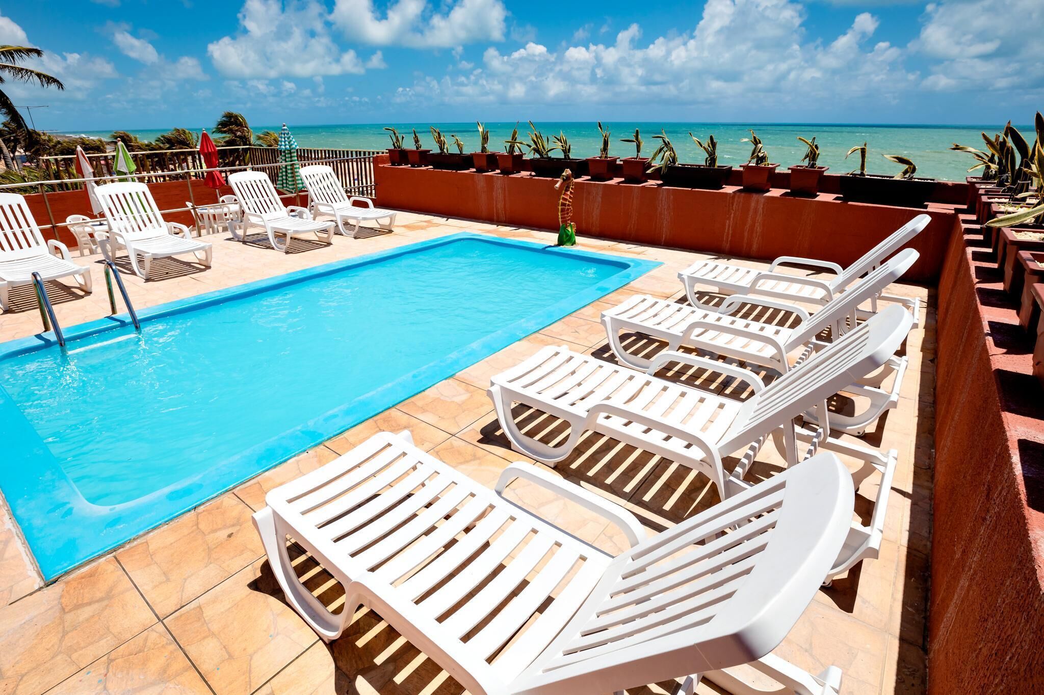 Zona de piscina con sillas reclinables blancas y vista al océano.