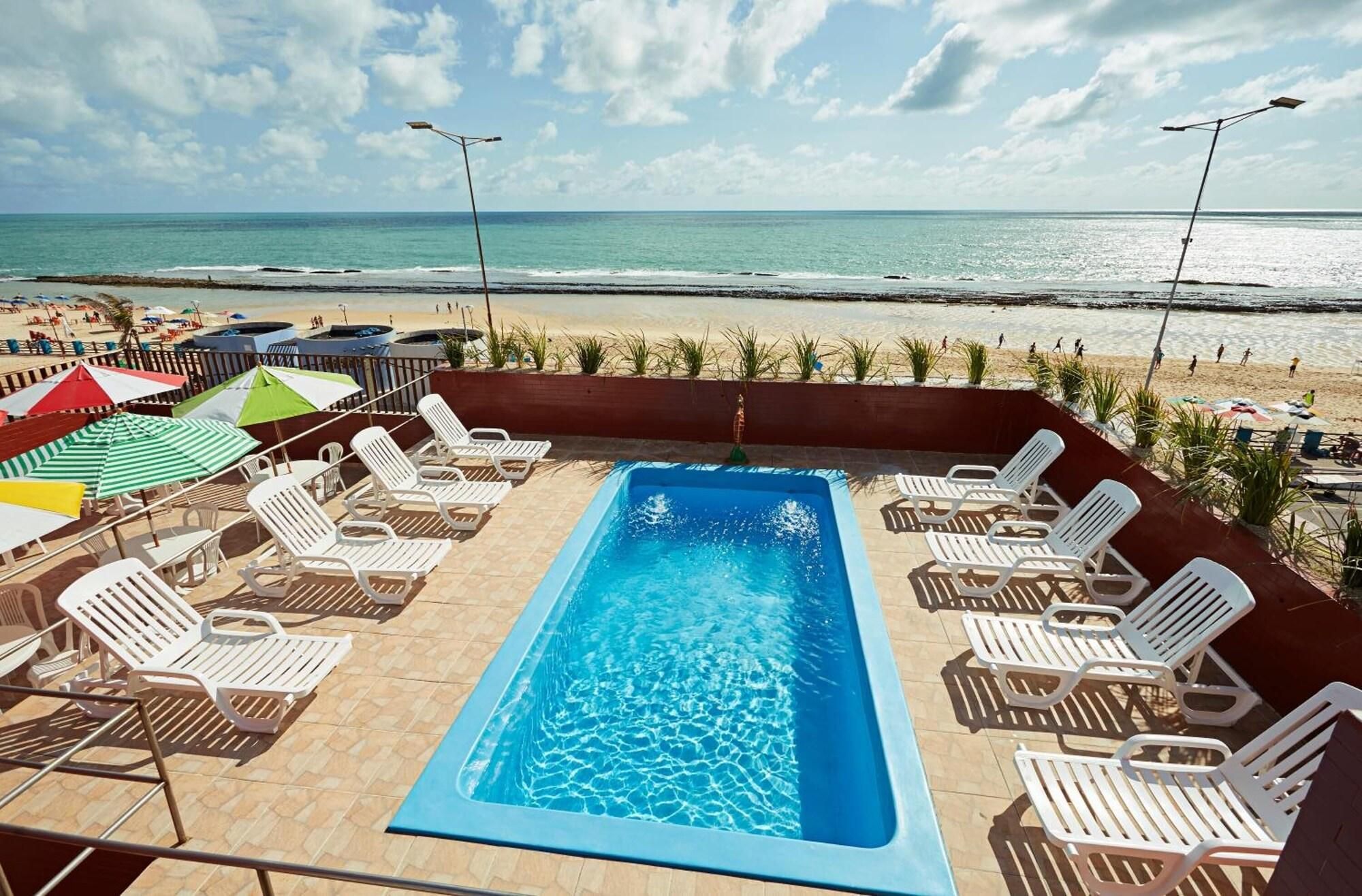 A swimming pool with lounge chairs and umbrellas, overlooking a beach.