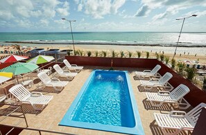 A swimming pool with lounge chairs and umbrellas, overlooking a beach.