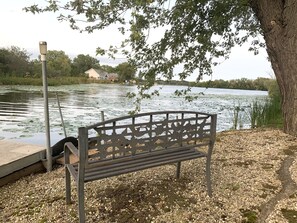 A bench by a lake with a dock and a tree. - Quiet Lakefront Oasiswith hot tub and boat rental (Trevor)