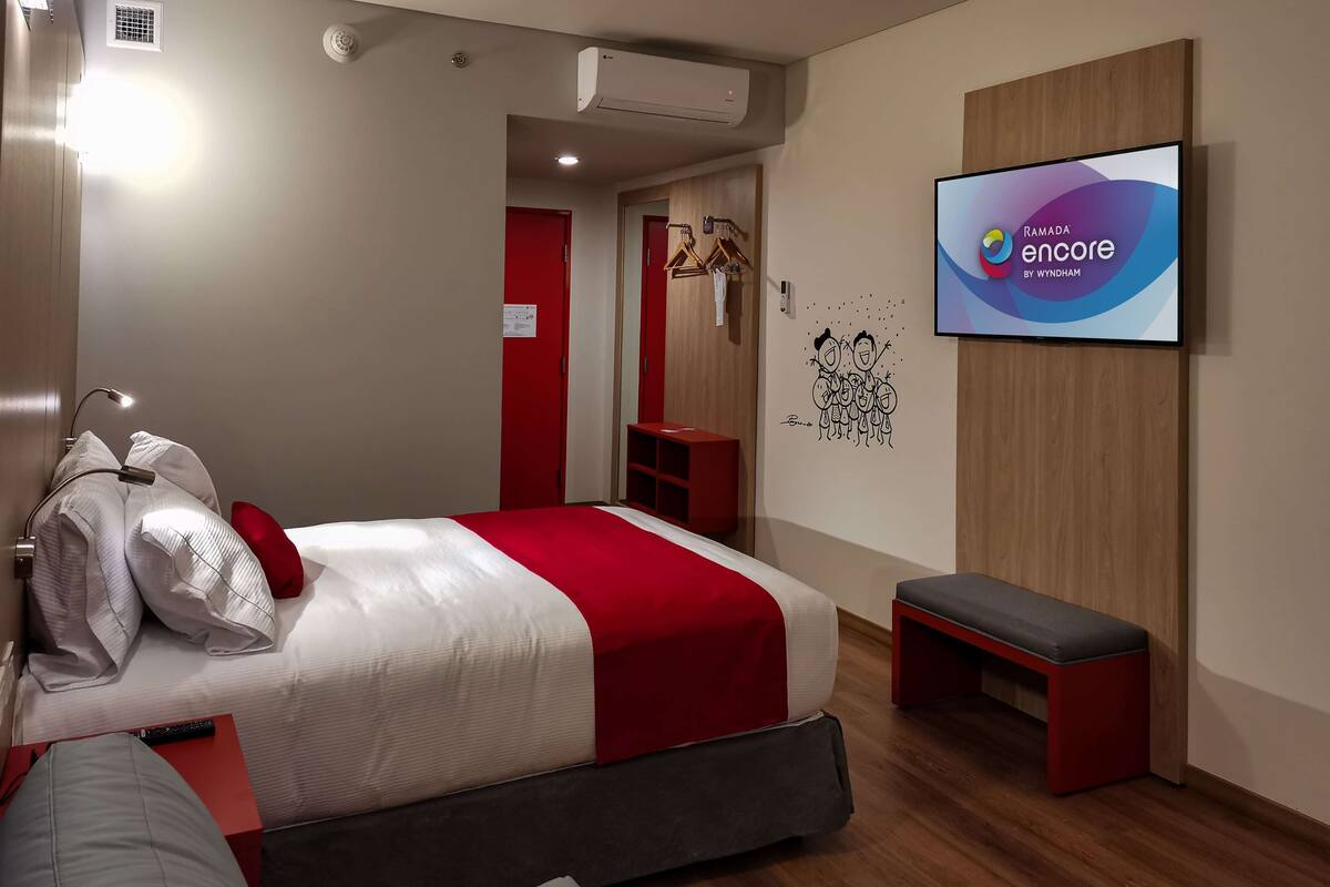 A modern hotel room with a bed, a bench, a TV, and a wardrobe.