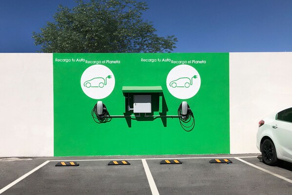 A parking area with a green wall featuring electric vehicle charging symbols and text. - Ramada Encore by Wyndham Monterrey Apodaca Zona Aeropuerto (Apodaca)