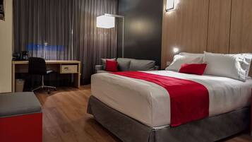 Quarto de hotel moderno com cama, escrivaninha, cadeira e um detalhe decorativo vermelho.