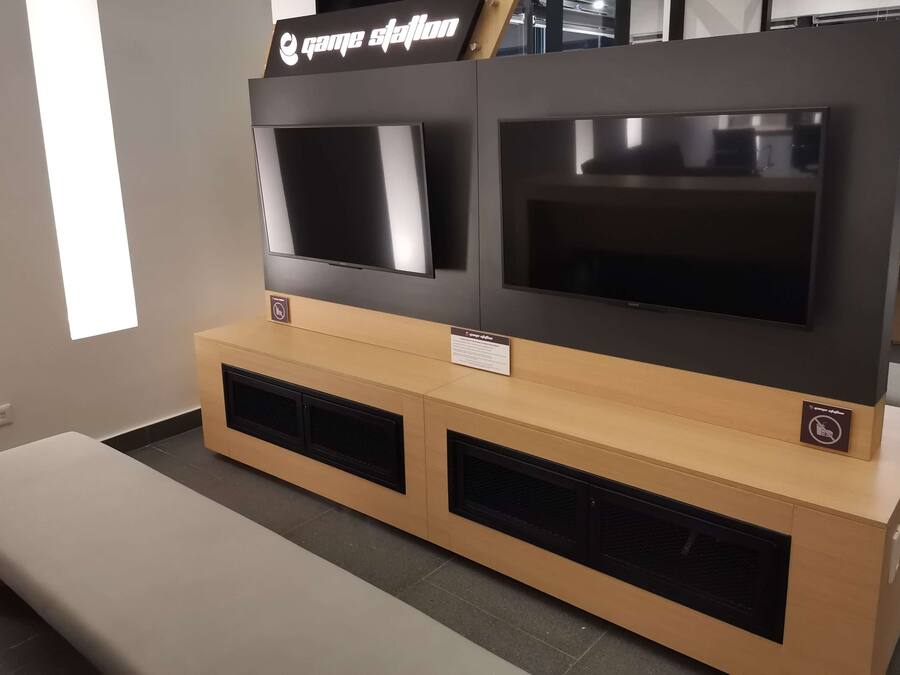 Ein Empfangsbereich mit einem Holztresen, zwei darüber montierten Fernsehern und einer Sitzbank im Vordergrund.