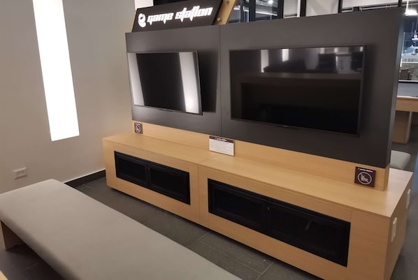 A reception area with a wooden counter, two televisions mounted above it, and a bench in the foreground. - Ramada Encore by Wyndham Monterrey Apodaca Zona Aeropuerto (Apodaca)
