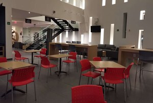 Una biblioteca moderna con sillas y mesas rojas, una escalera y un cartel que indica 'Conferencia de Ciencias Sociales'.