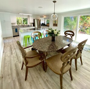 A modern kitchen with white cabinets, a stainless steel refrigerator, and a granite countertop. There is a dining area with a round table and wooden chairs. - SeaTurtle đ˘Bayfront w/ heated pool, steps to Beach, Sleeps 10, Petsđž (Englewood)