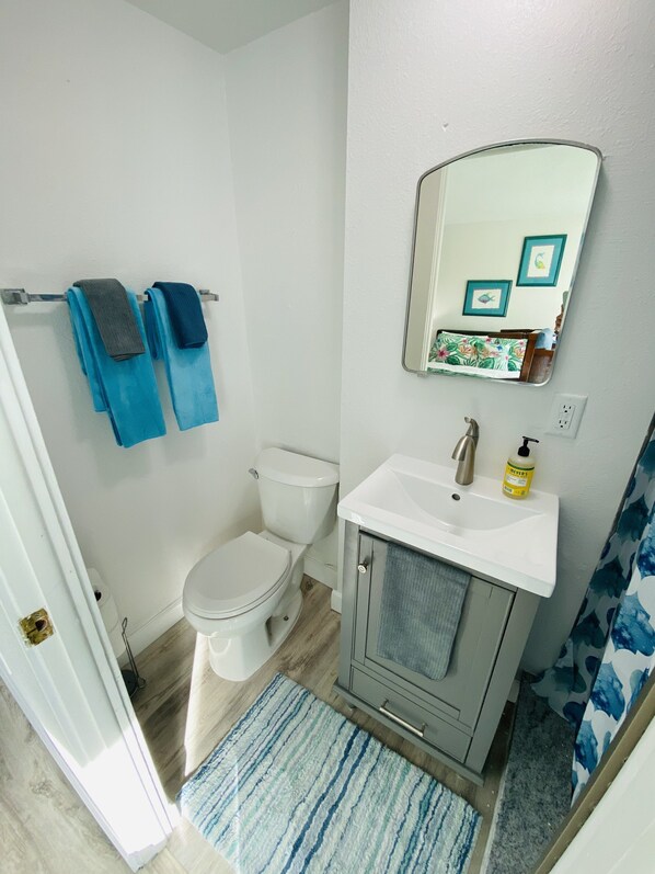 A bathroom with a toilet, sink, and mirror. There are towels hanging on a rack and a rug on the floor. - SeaTurtle 🐢Bayfront w/ heated pool, steps to Beach, Sleeps 10, Pets🐾 (Englewood)