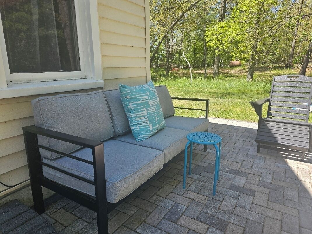 Un patio con un sofá gris, una mesita azul pequeña y una silla de madera.