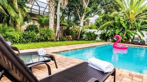 Un área de piscina con sillones reclinables, una mesa de vidrio y un flotador con forma de flamenco.
