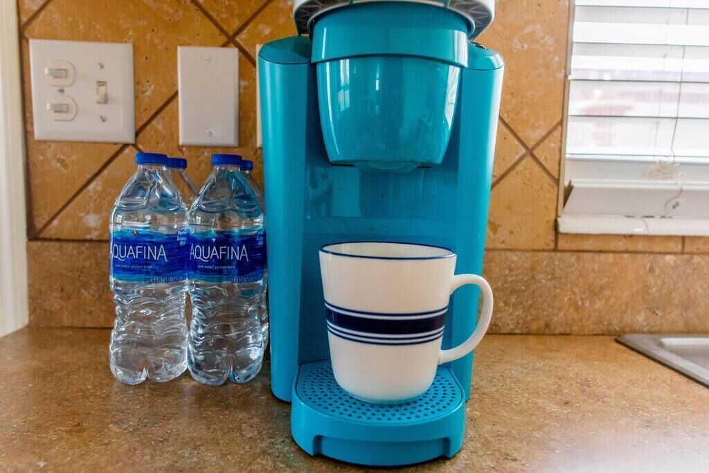 A kitchen counter with a blue coffee maker, two water bottles, and a white mug.