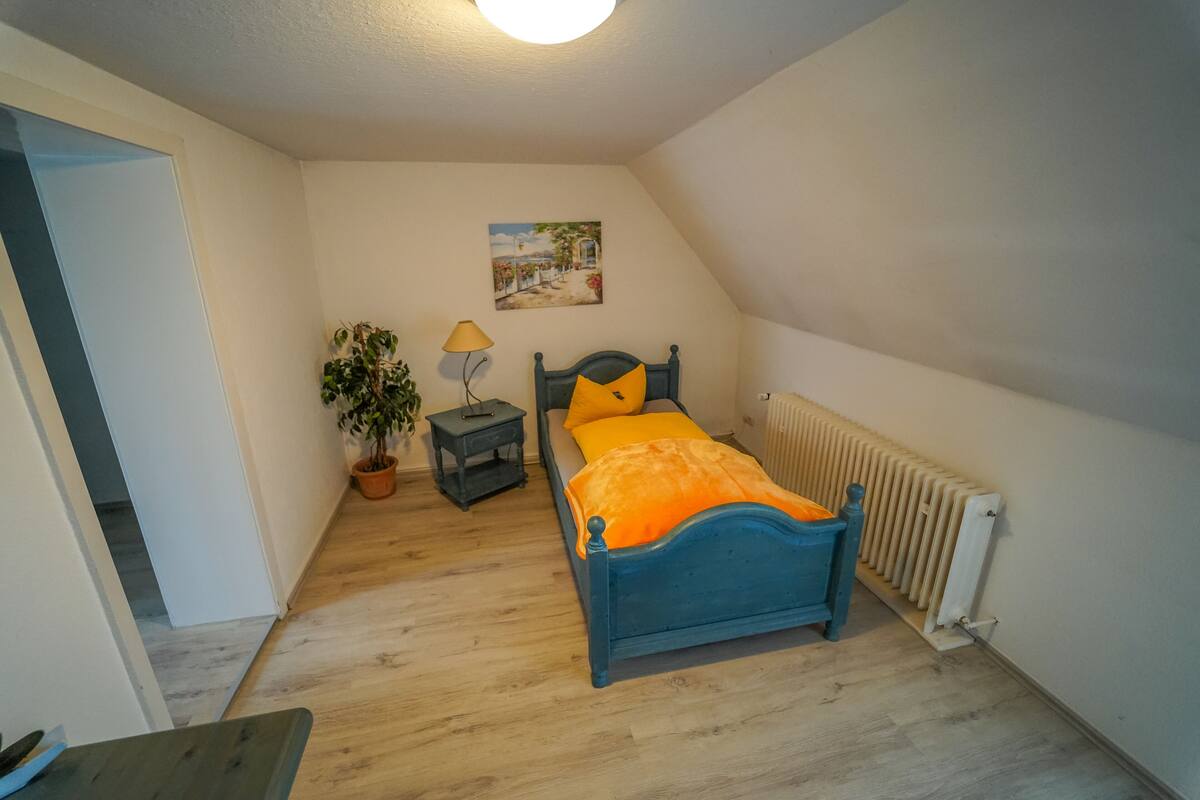 A bedroom with a bed, a nightstand, a potted plant, a lamp, and a radiator.