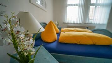 A bed with blue bedding and two yellow pillows, a bedside table with a lamp, and a potted orchid plant.