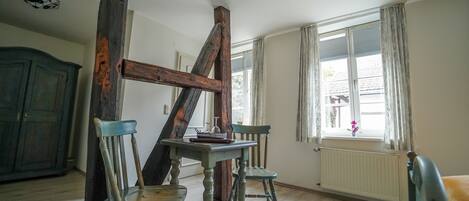 Una habitación con estructura de vigas de madera, una mesa, dos sillas, un radiador y un ventanal con cortinas.