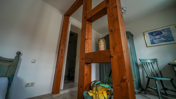 Una habitación con una estructura de escalera de madera, una silla, una mesita y un cuadro en la pared.