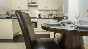 A modern kitchen with white cabinets, a gas stove, and a dining area with a glass table set for two. - No 5 Central by Brighton Holiday Lets (Brighton)