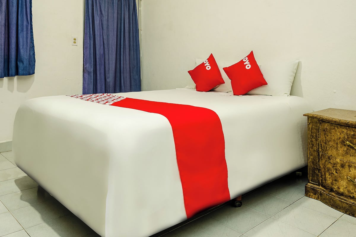 A neatly made bed with a white and red bedspread, two red pillows, and a wooden nightstand beside it.
