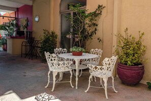 Un patio al aire libre con una mesa redonda y sillas de metal blanco, rodeado de plantas en macetas.