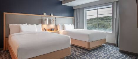 A hotel room with two beds, a large window with a view, and a patterned carpet.