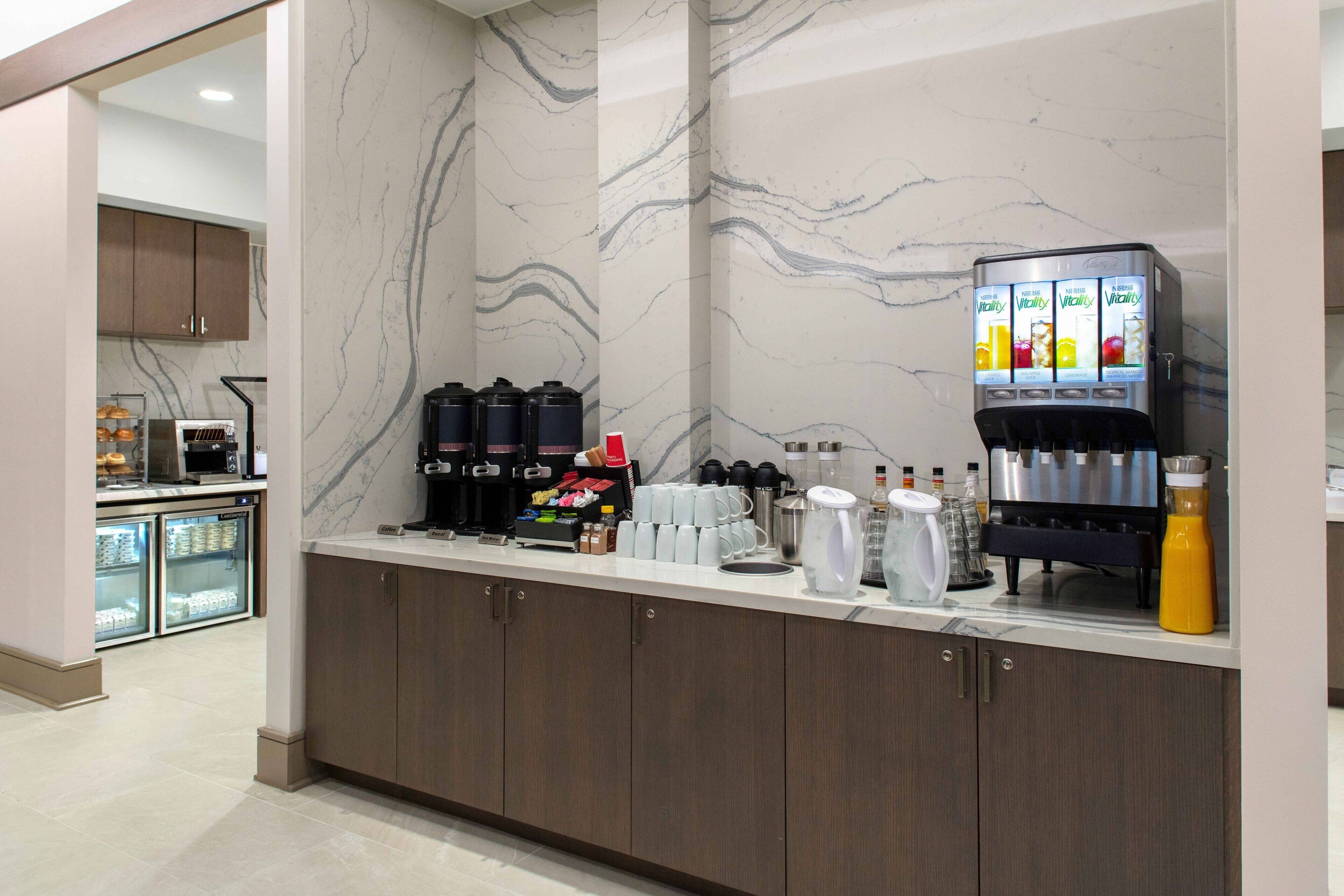 A modern kitchen area with marble countertops, a coffee machine, and a beverage dispenser.