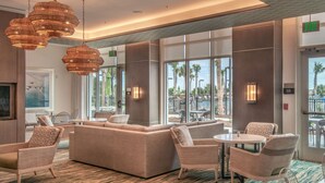 A modern lobby with a large seating area, large windows, and a view of palm trees outside. - Residence Inn by Marriott Jekyll Island (Jekyll Island)