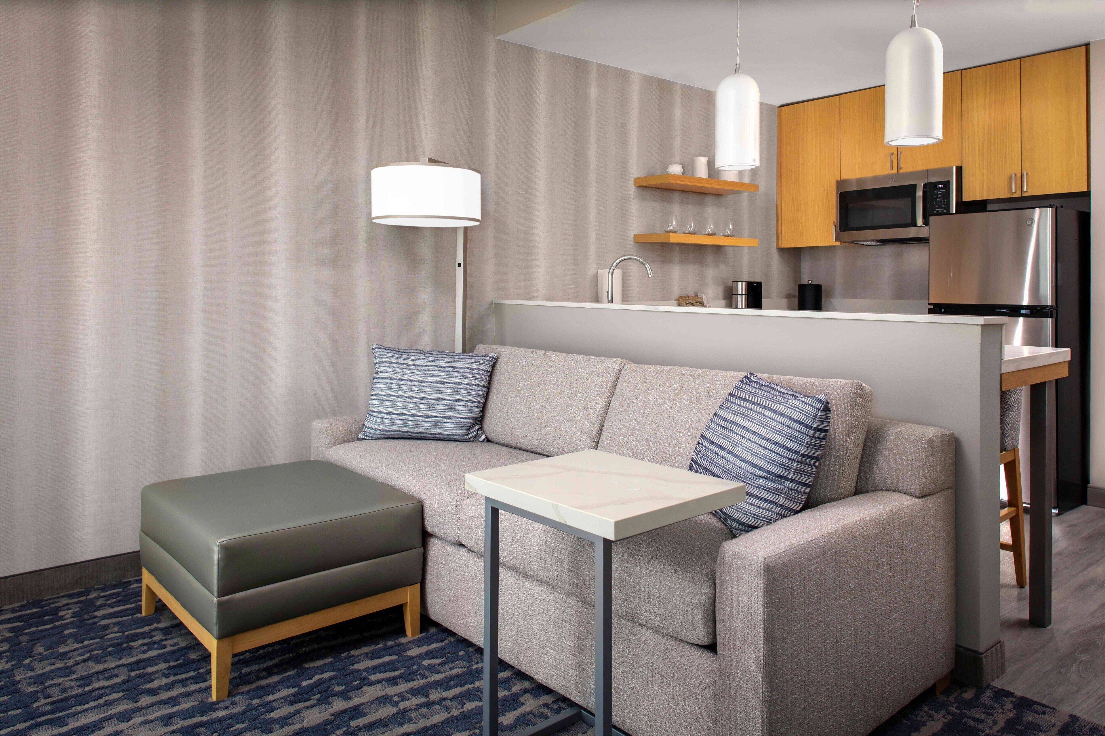A modern hotel room with a sofa, ottoman, and a small table.