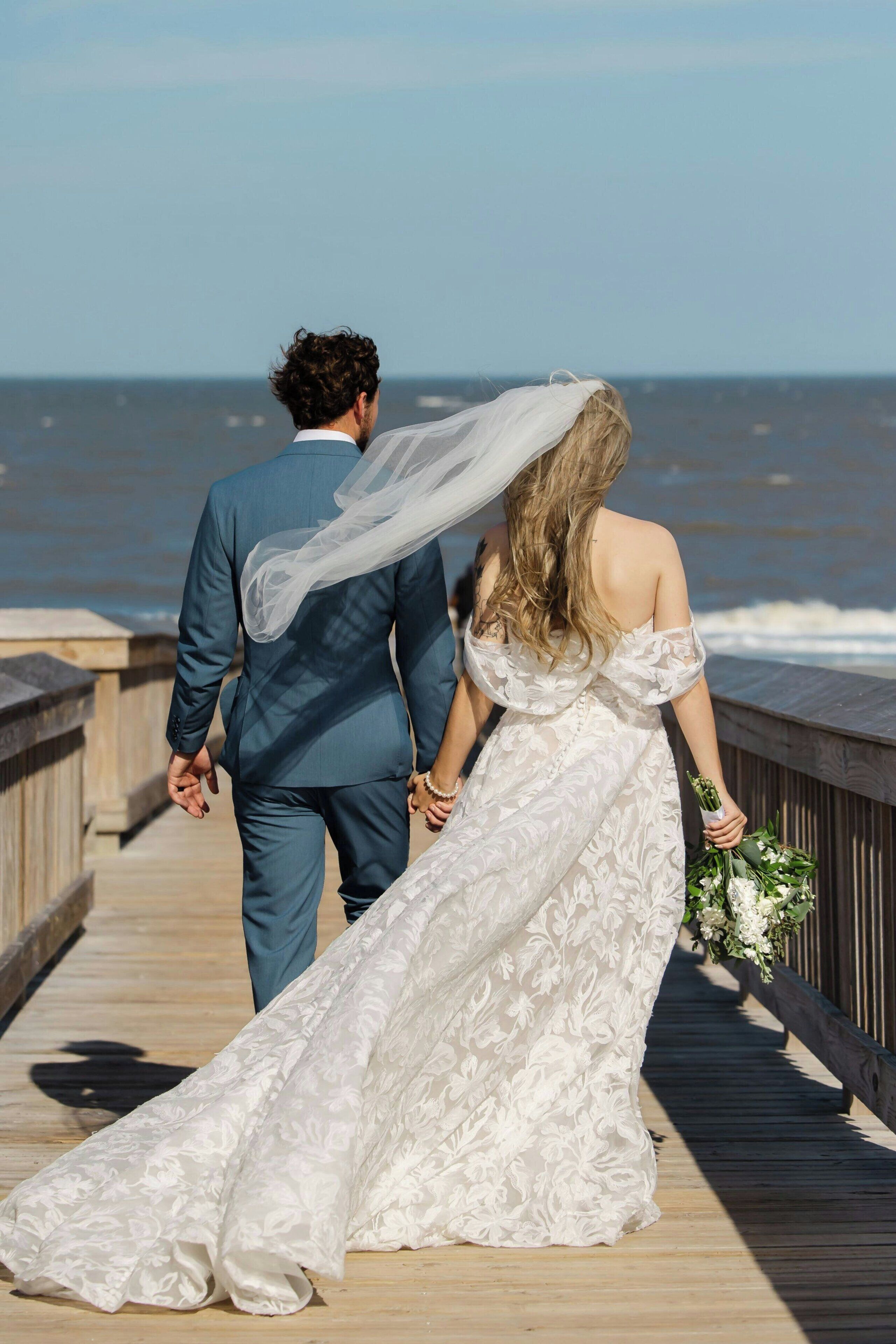A couple walking on a wooden pier with a view of the ocean.