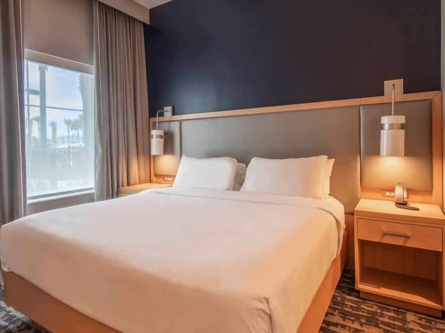 Hotelkamer met een groot bed, een nachtkastje met lamp en uitzicht op palmbomen door het raam.