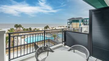 A balcony with a view of a swimming pool, beach, and adjacent buildings.