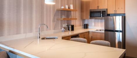 A modern kitchen with a marble countertop, stainless steel appliances, wooden cabinets, and pendant lighting.
