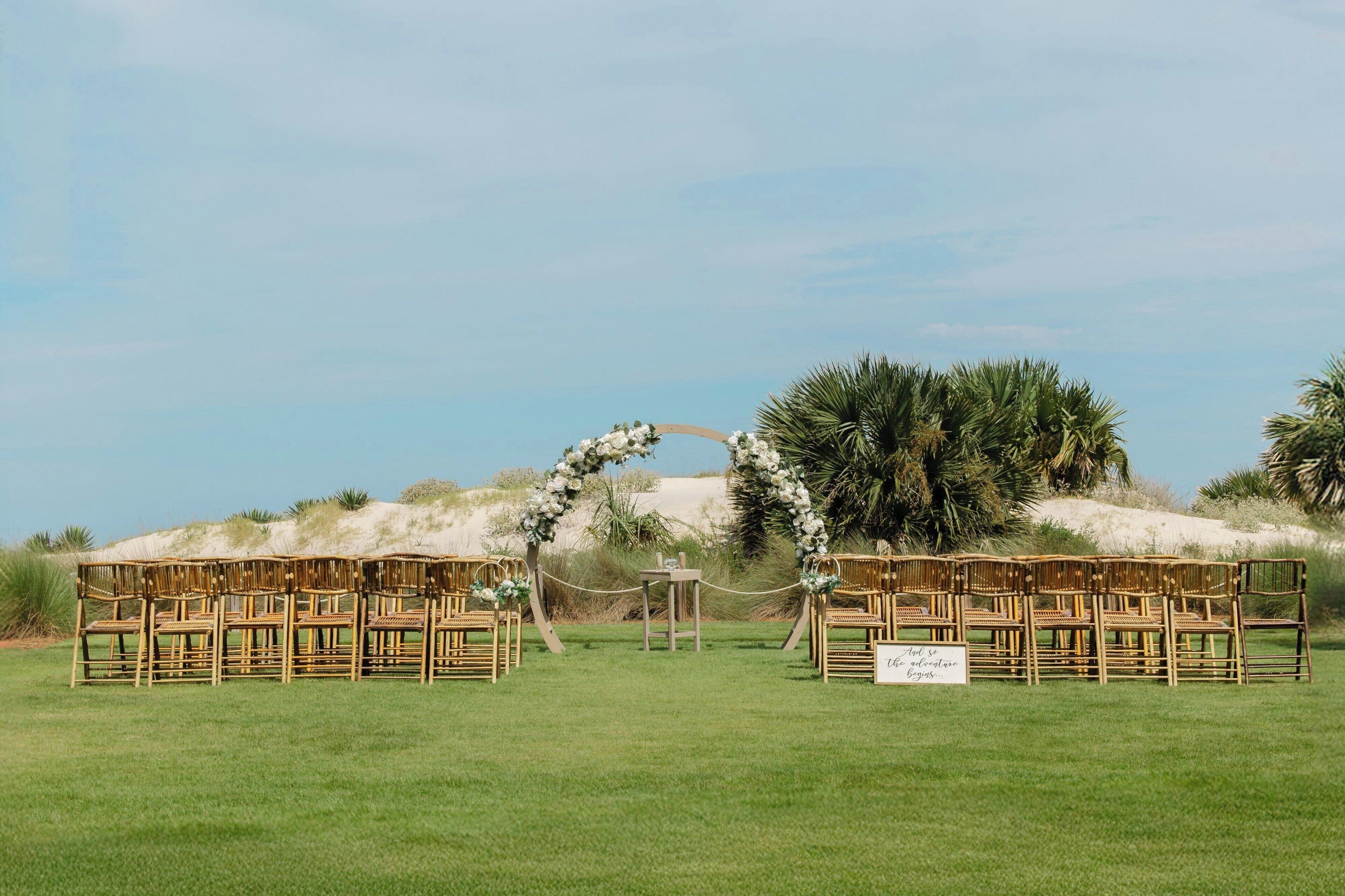 A wedding ceremony setup with a floral arch and bamboo chairs.