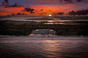 A coastal landscape with a sunset, a beach, and a large building with multiple stories.