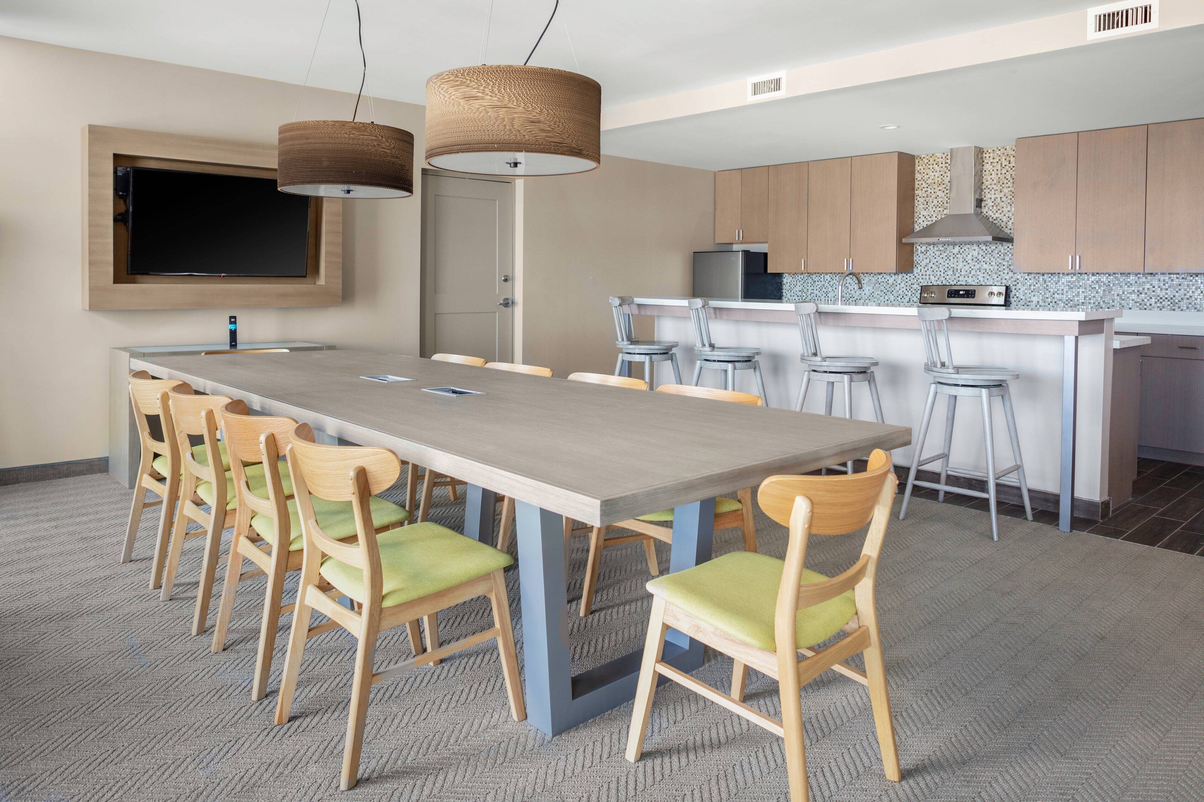 A modern kitchen with a central island, bar stools, and a flat-screen TV mounted on the wall.