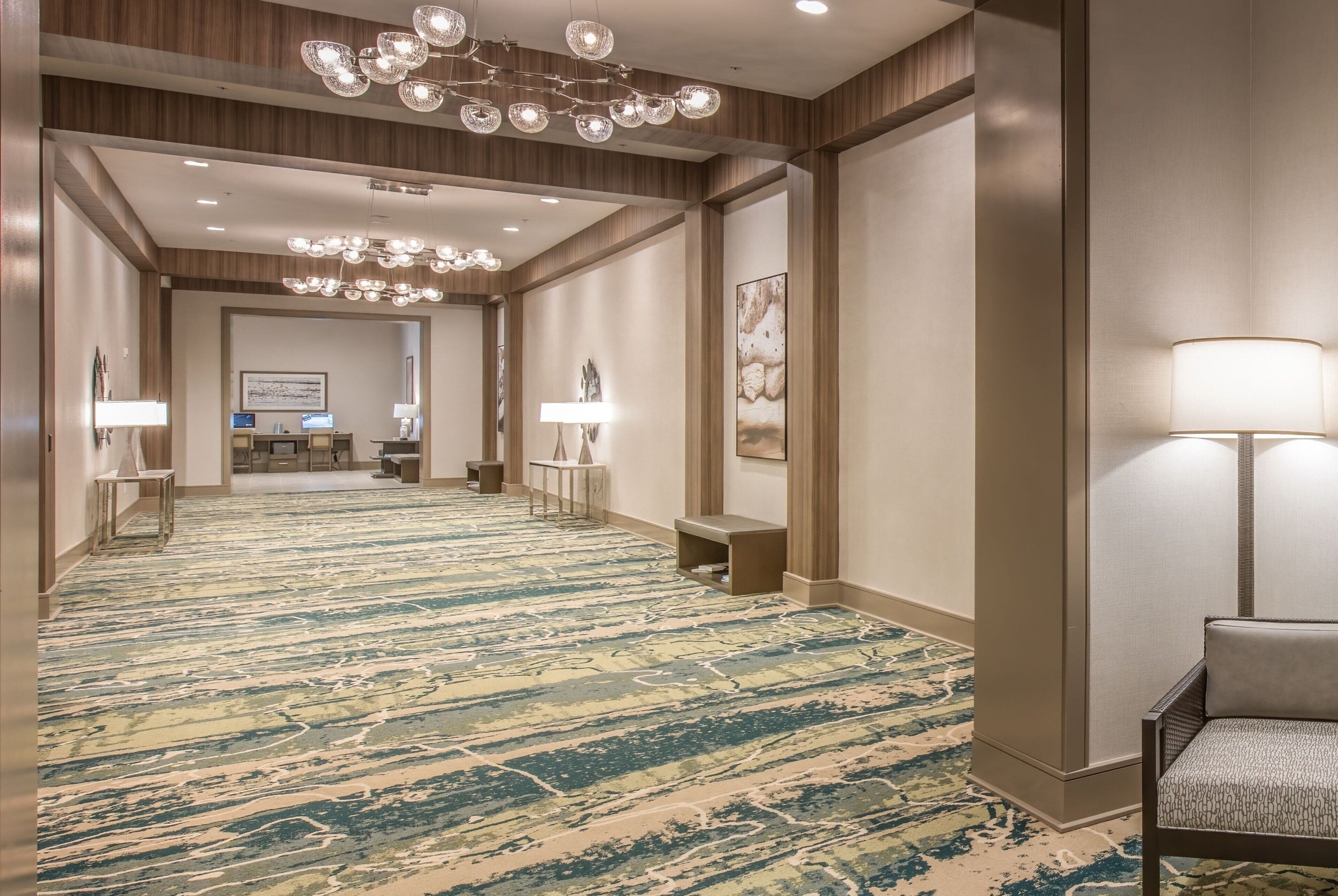 A hotel hallway with a patterned carpet, a reception desk, and a seating area with a lamp.