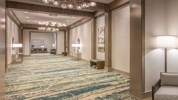 Un pasillo de hotel con alfombra estampada, una recepción y una zona de estar con lámpara.