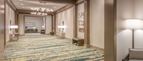 A hotel hallway with a patterned carpet, a reception desk, and a seating area with a lamp.