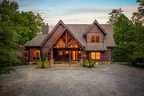 A large, two-story log cabin with a prominent front porch, multiple windows, and a gravel driveway. - Secluded, Modern Cabin, Views, Lake, Private Dock, Starlink Speed WIFI (Topton)