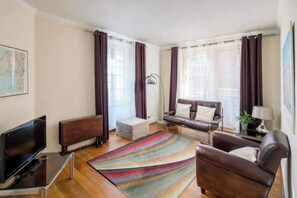 Un salon avec un canapé, des fauteuils, un téléviseur et une lampe sur pied.