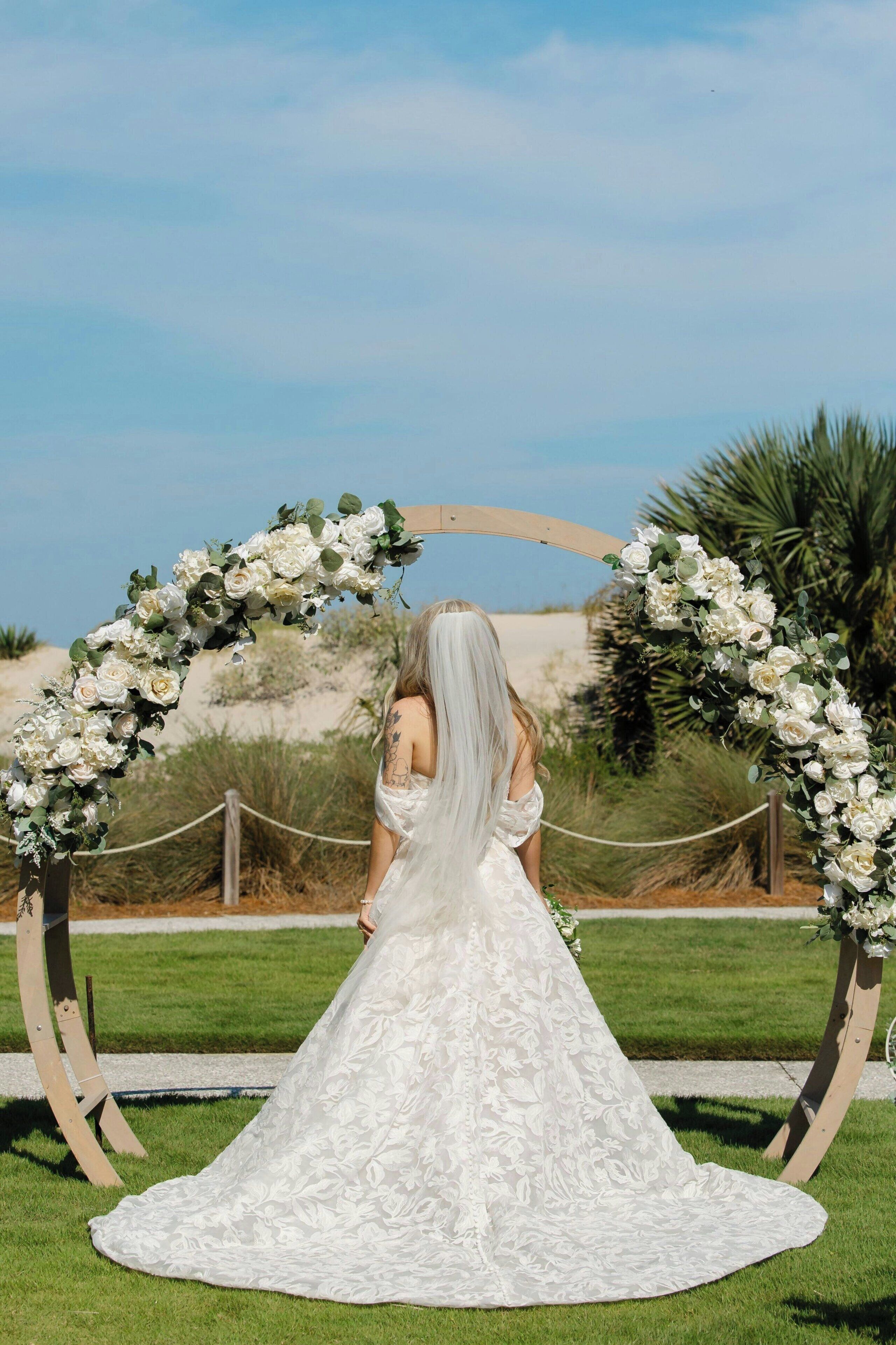 A wedding ceremony setup with a floral arch and a bride in a white dress.